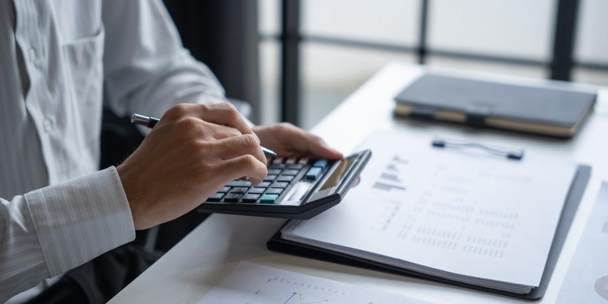 Professional calculating costs for a Medicare cost report using a calculator and financial documents at a desk. 